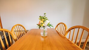 Una mesa de comedor de madera con un jarrón de flores en el centro, rodeada de sillas de madera.