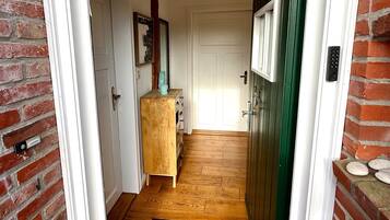 Ein Flur mit Holzboden, einer schwarzen Matte am Eingang, einem Holzschrank und einer grünen Tür.