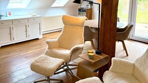 Amplio dormitorio tipo loft con techo alto, vigas de madera, tragaluces, una zona de estar acogedora con sillones mullidos, una mesita y vistas a zonas verdes.