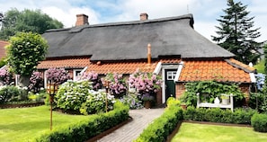 A traditional house with a thatched roof, brick walls, and a well-maintained garden with various plants and flowers.