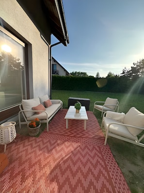 A patio with a white sofa, two white chairs, a small table, and a red patterned rug.