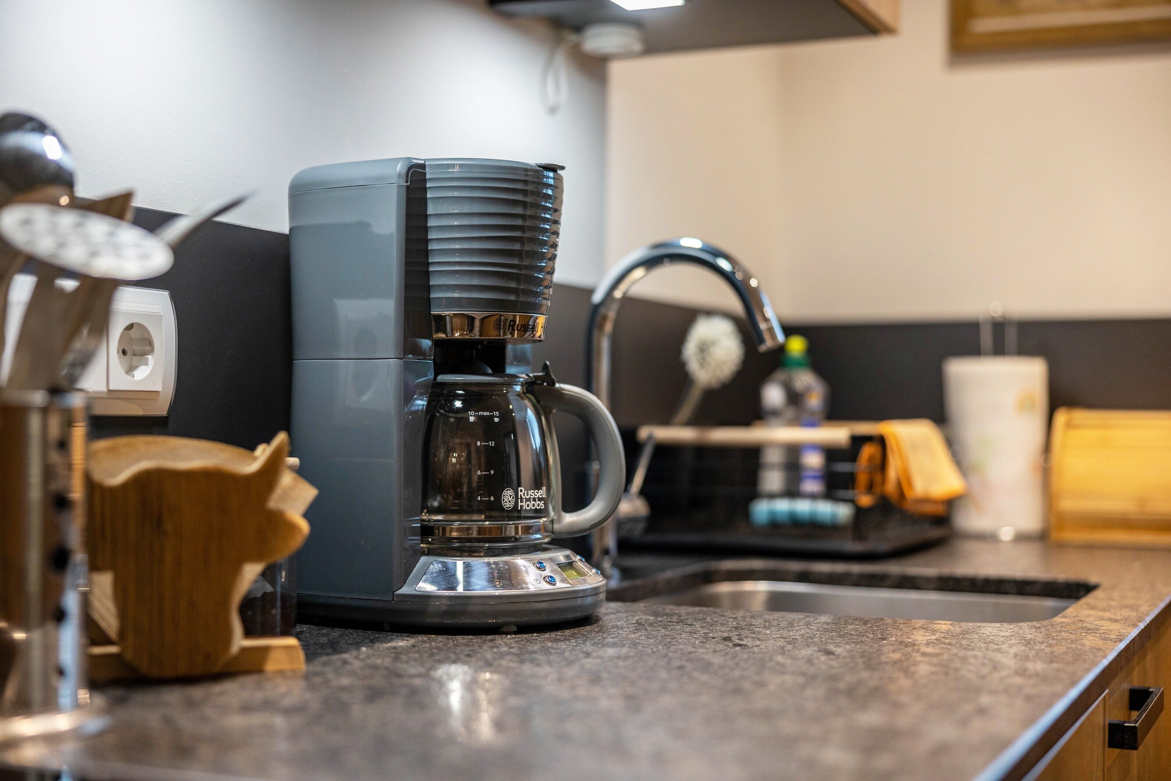 Eine Küche mit einer Kaffeemaschine, einem Wasserhahn und einem Holz-Küchenhelfer-Halter.