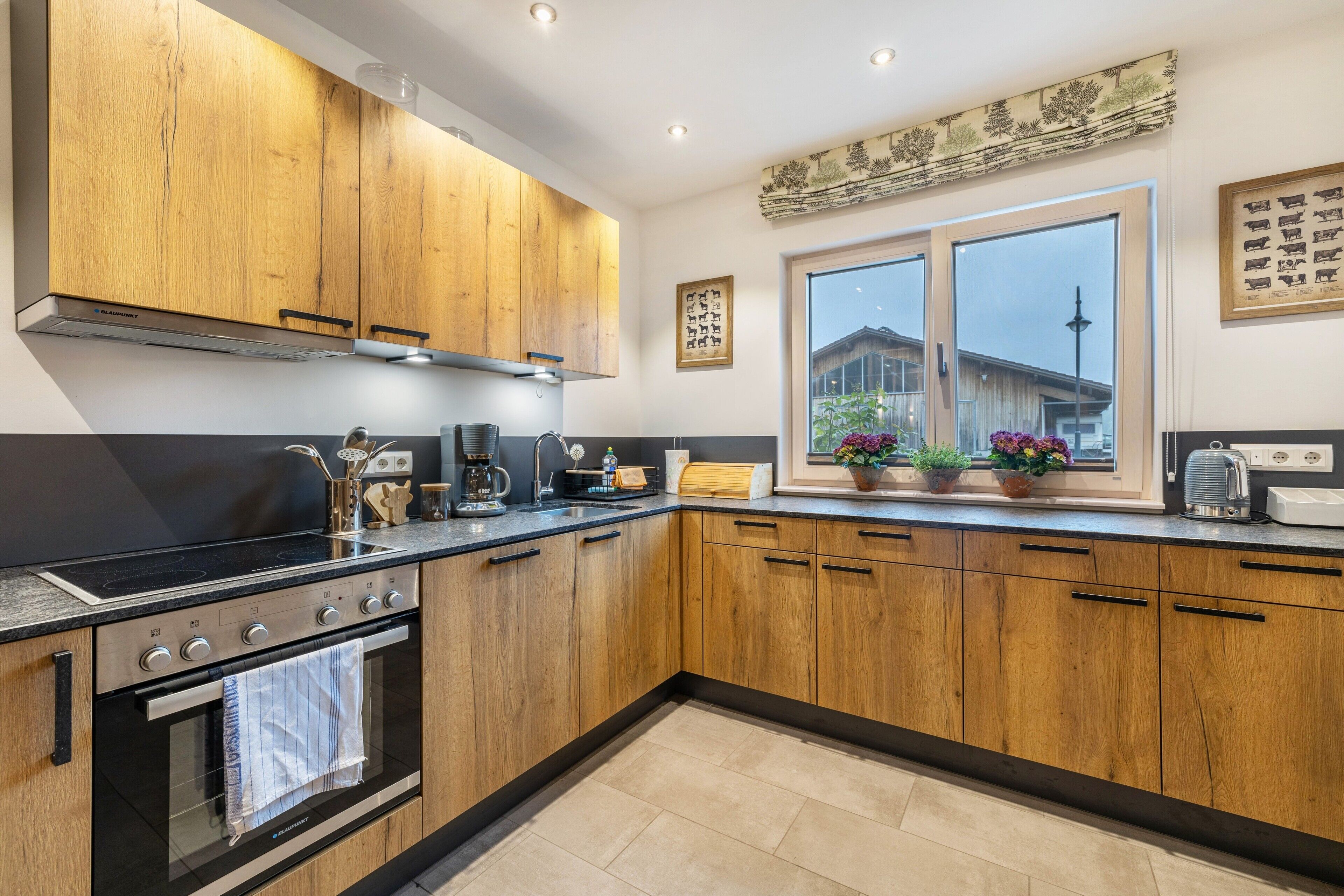 Una cocina moderna con armarios de madera, horno empotrado y ventana con vistas a una casa.