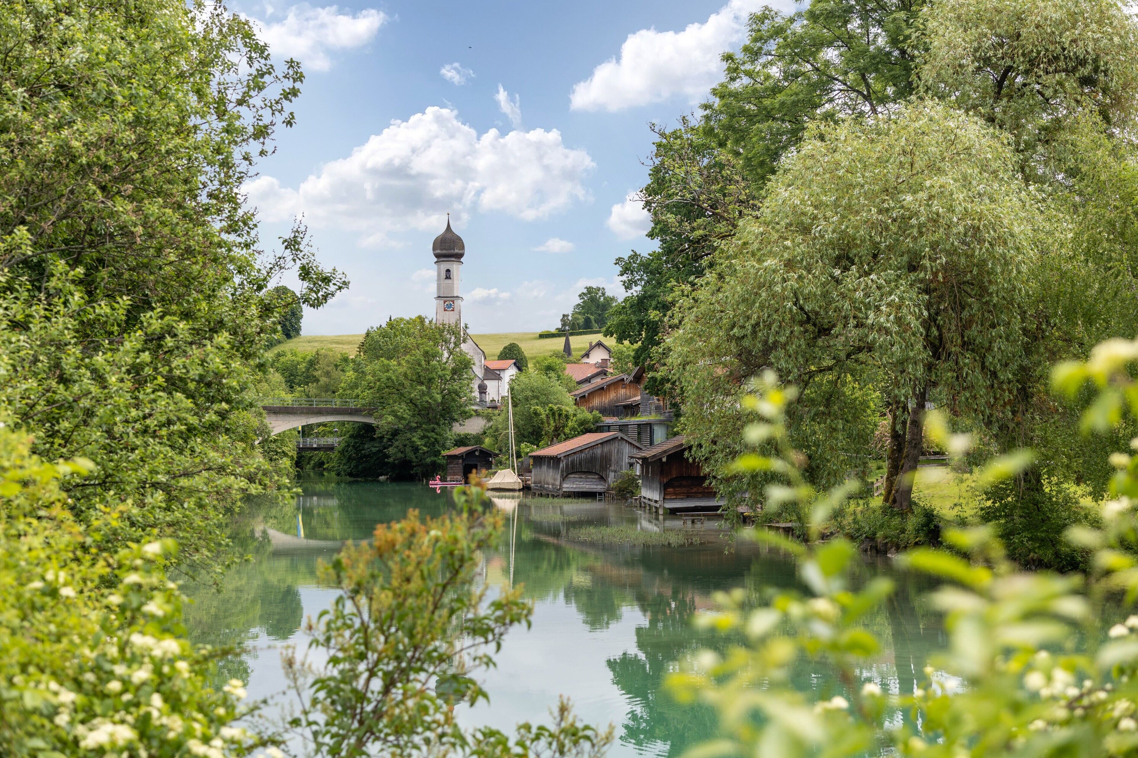 A serene riverside village with traditional architecture, a bridge, and a church tower.