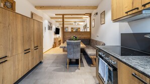 Une cuisine moderne avec des meubles en bois, un four encastré et un coin repas comprenant une chaise grise et une table en bois.