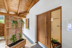 A wooden door with a number plate, a wooden slatted structure with plants, and a potted plant on the ground.