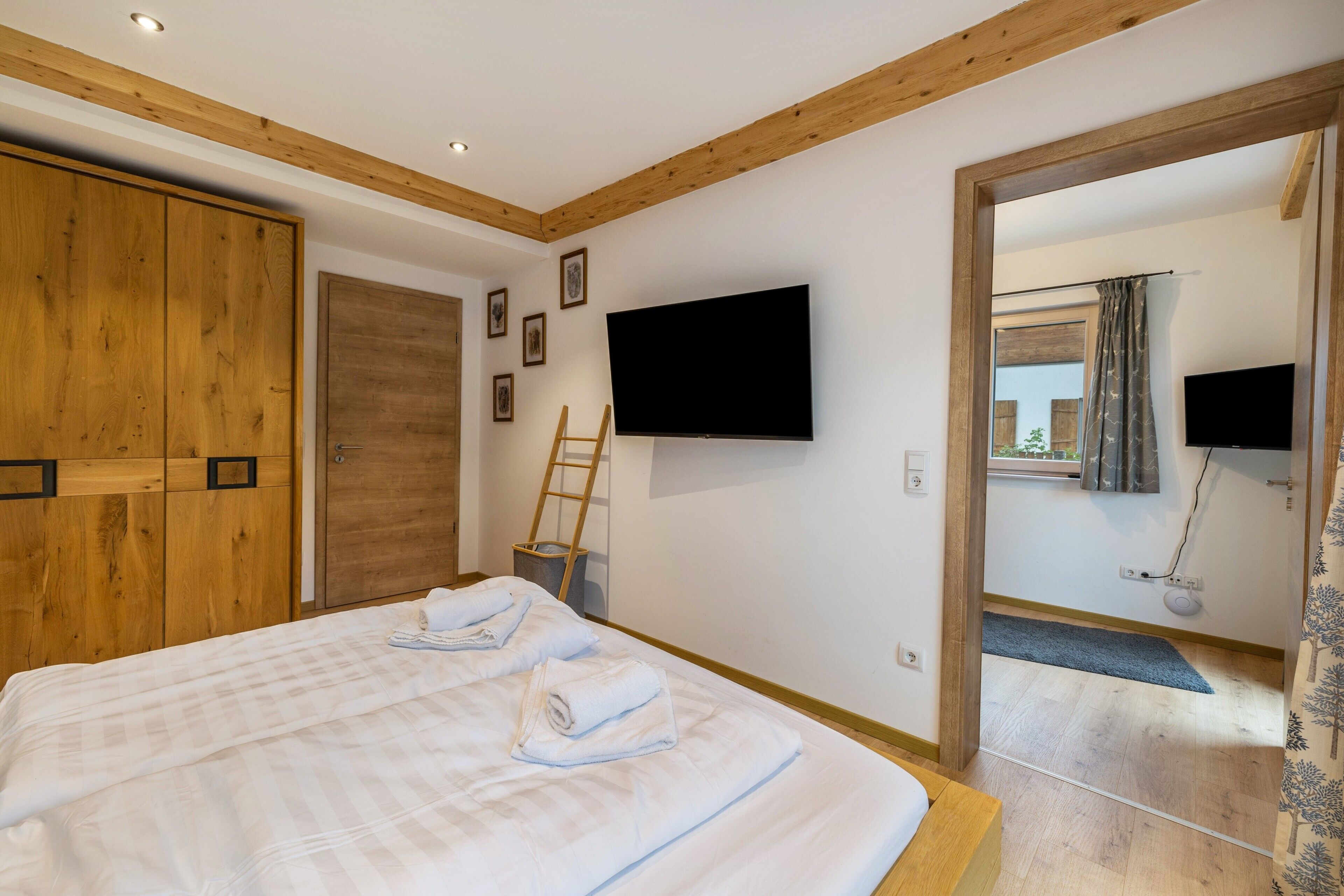 Ein Schlafzimmer mit einem großen Bett, einem Holzschrank, einem an der Wand befestigten Fernseher und einer Tür zu einem anderen Raum.
