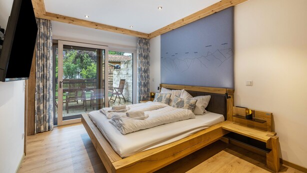 Une chambre avec un lit en bois, un téléviseur à écran plat, une grande fenêtre et une vue sur l’extérieur.