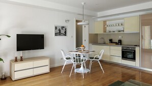 Una cucina moderna con mobili bianchi, un tavolo da pranzo con sedie, un televisore a schermo piatto e una piccola pianta.