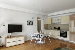 A modern kitchen with white cabinets, a dining table with chairs, a flat-screen TV, and a small plant. - Oliva Boutique Apartment 2 (Dubrovnik)