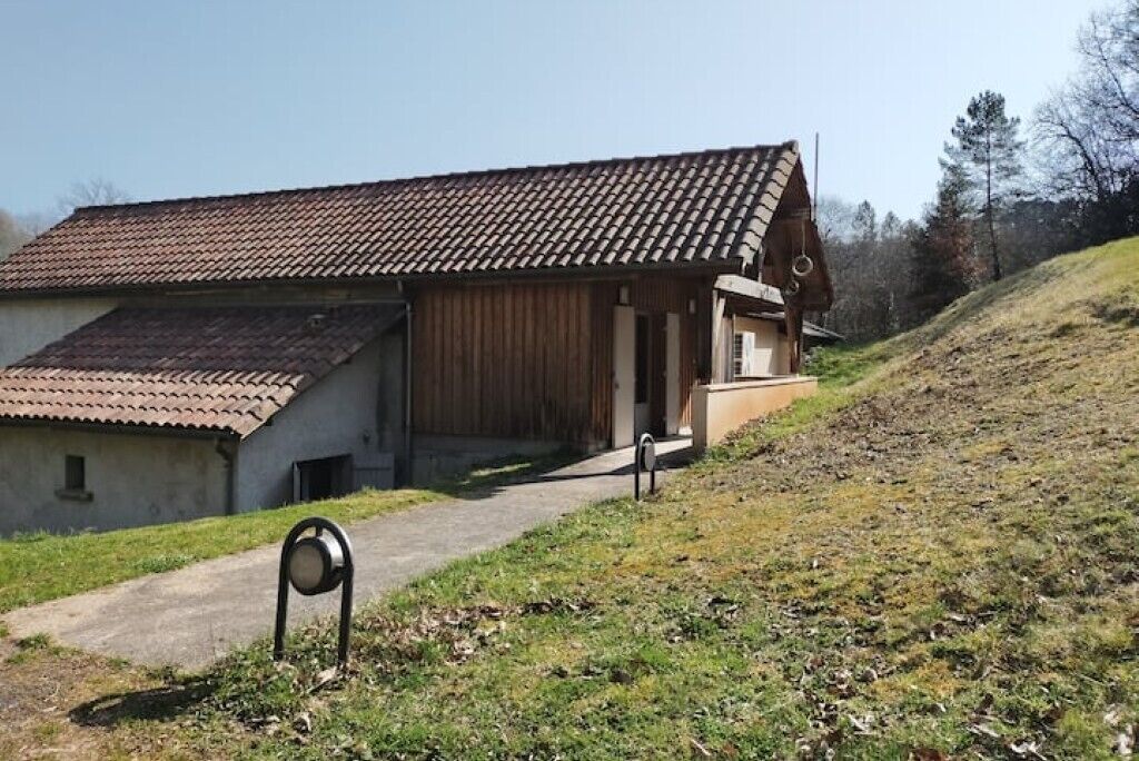 Un bâtiment rustique, doté d’un toit en tuiles et d’une façade en bois, situé sur une pente herbeuse.