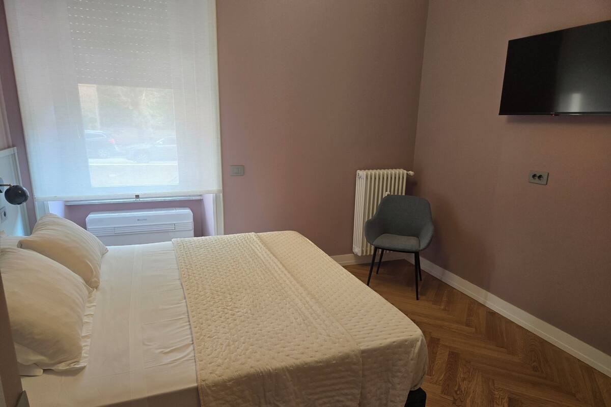 Une chambre à coucher avec un lit, une chaise, un radiateur et un téléviseur fixé au mur.