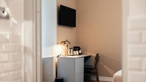 Een compacte kamer met een kitchenette, een wandtelevisie, een lamp en een stoel.
