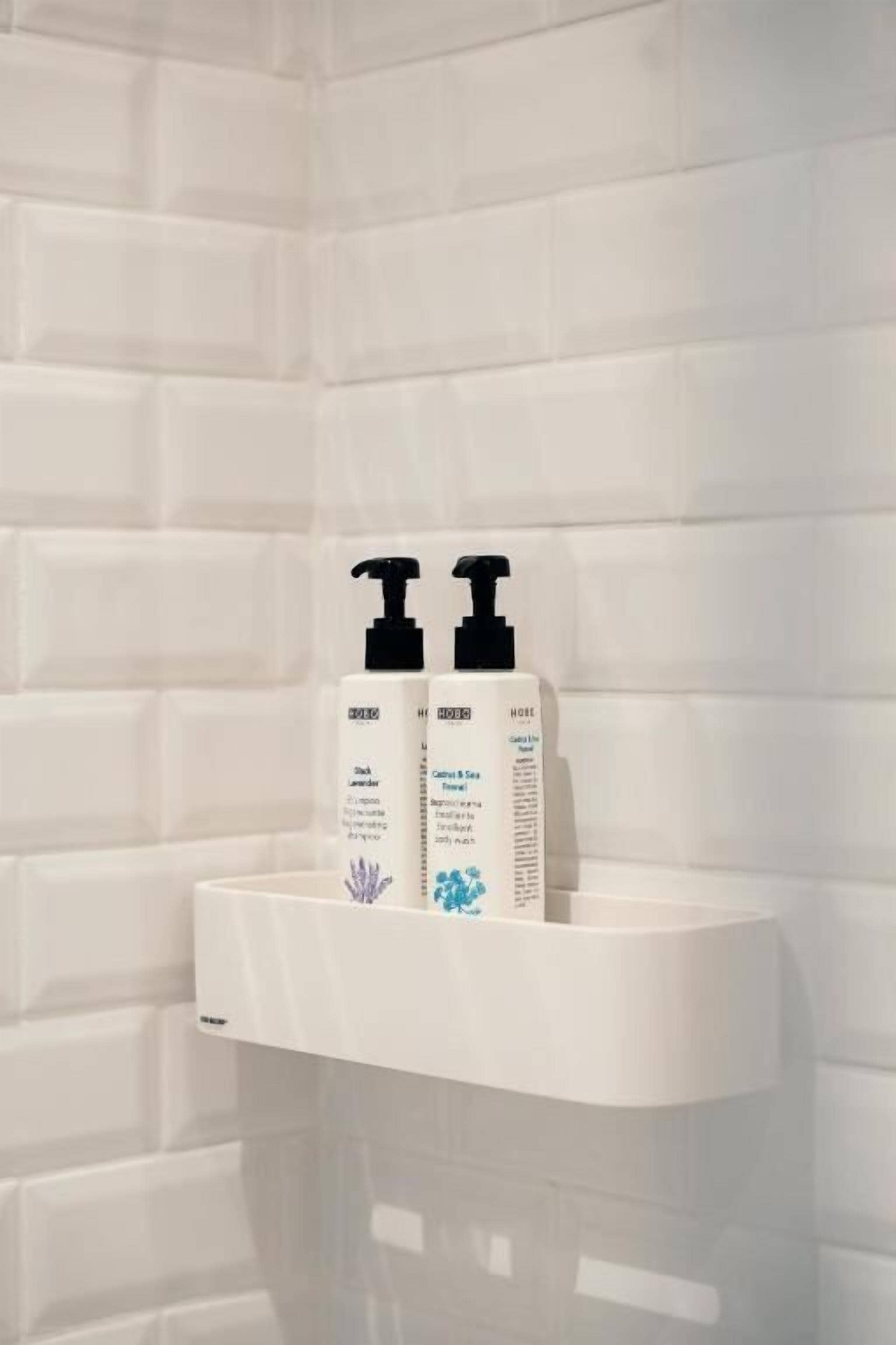 A bathroom with a white tiled wall and a white sink. There are two bottles of shampoo and conditioner on the sink.