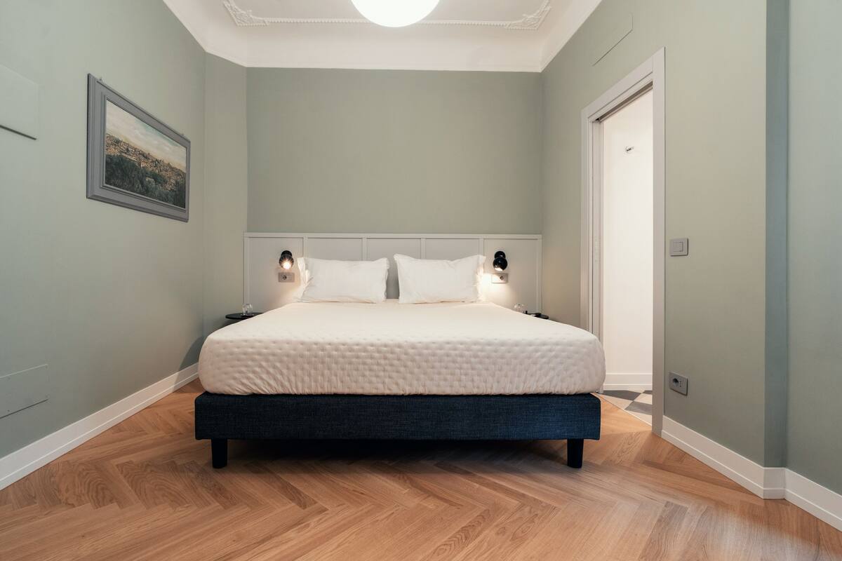 Une chambre à coucher avec un lit, deux lampes de chevet, une table de nuit et un tableau encadré au mur.