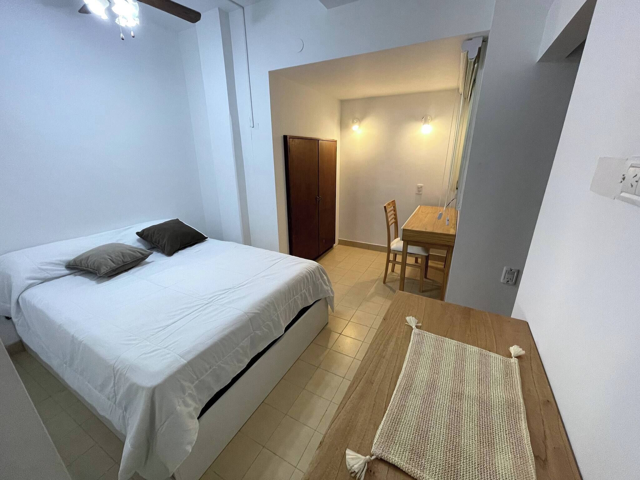 Un dormitorio pequeño y bien iluminado con una cama, una mesa de madera y una silla.