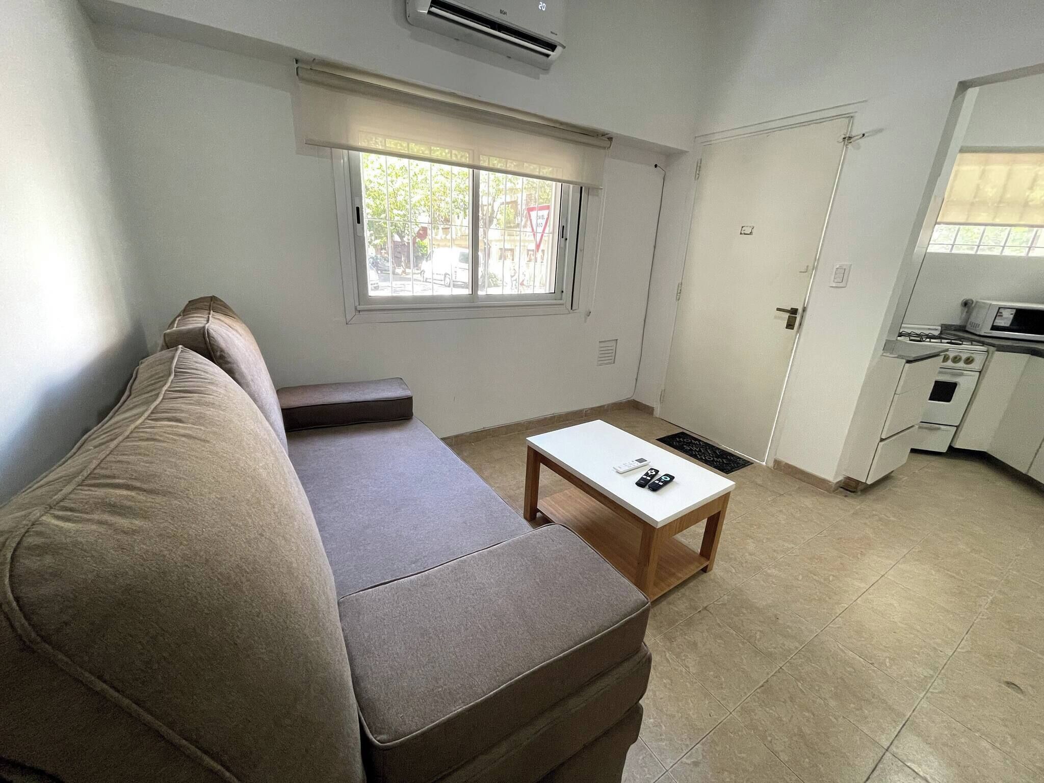 A compact living space with a sofa, a small table, a window, and a kitchenette.