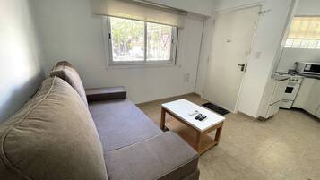 A compact living space with a sofa, a small table, a window, and a kitchenette.