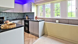 A modern kitchen with a herringbone floor, a built-in oven, and a window with a view of greenery. - River View Cottage (Skipton)
