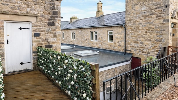 A stone building with a wooden deck and a white door. - River View Cottage (Skipton)