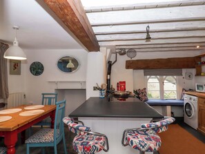 Une cuisine compacte dotée d’un îlot central, d’un lave-linge et d’un coin repas avec une table en bois et des chaises bleues.