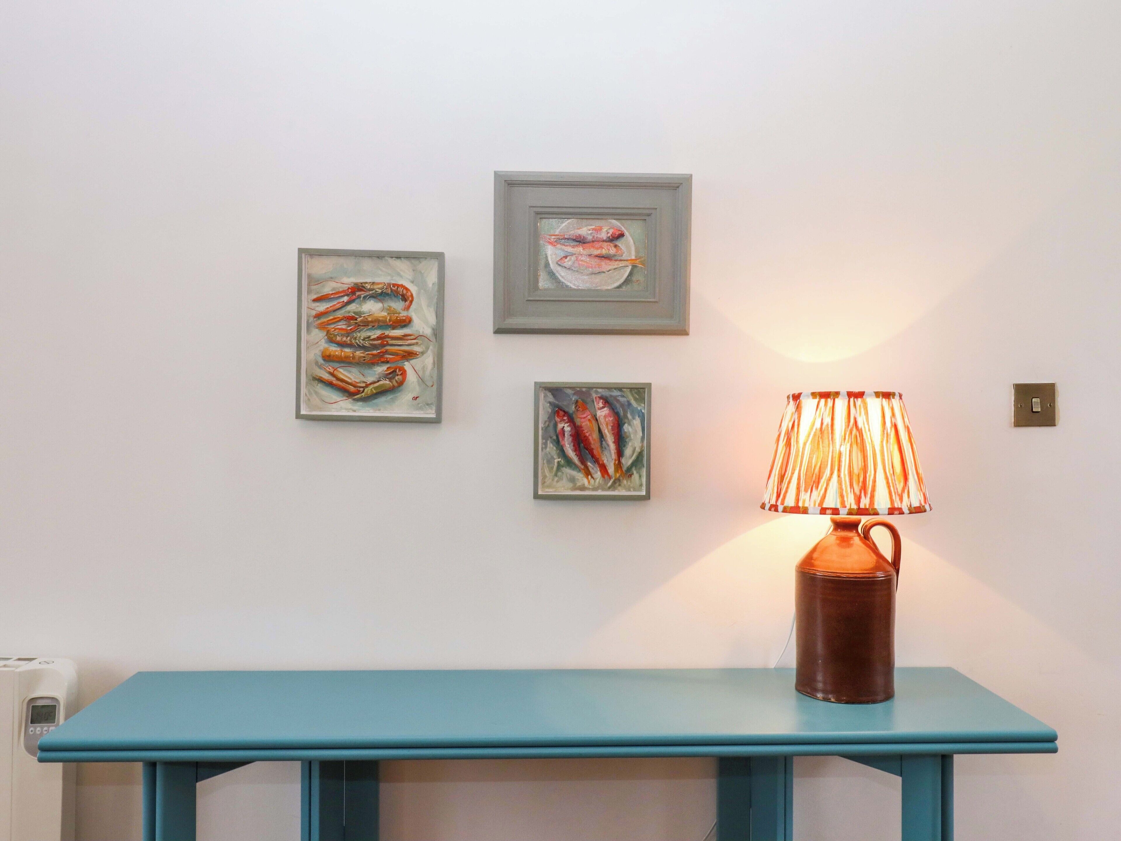 A teal table with a lamp and three framed artworks on the wall.