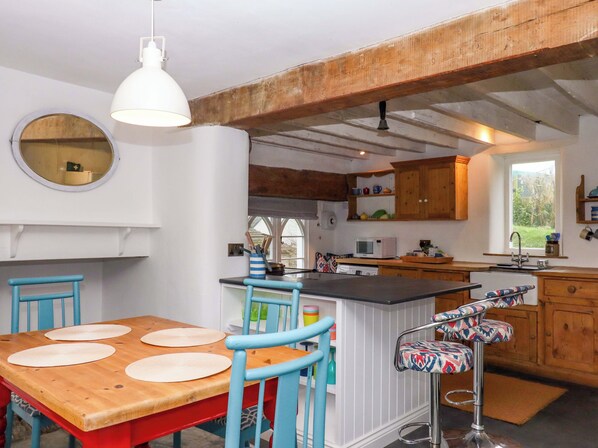 Une cuisine avec un îlot central en bois, des chaises bleues, un miroir rond et un luminaire suspendu.