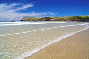A beach with clear blue water, sandy shore, and grassy hills in the background.