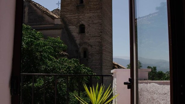 Een balkon met een bloempot, uitzicht op een historische toren en een heldere lucht.