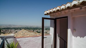 Een balkon met uitzicht op een stadslandschap, een witte muur en een pannendak.