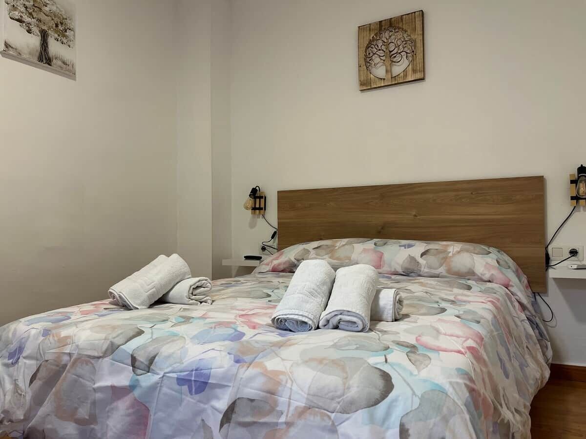 Uma cama bem arrumada com colcha estampada e duas toalhas enroladas sobre ela.
