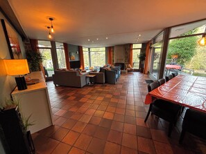 A spacious living area with a fireplace, large windows, and a dining table. - Heyen Estate (Waimes)
