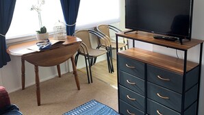 Habitació amb escriptori de fusta, cadires de vimet, televisió sobre un suport i un armari d'arxiu negre gran.