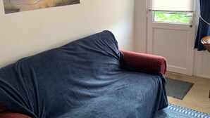 Habitació amb un sofà blau, un quadre d'una escena de platja, una finestra amb persianes i una porta amb felpú.