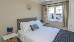 Ein Schlafzimmer mit einem Bett, zwei Nachttischen, einer Lampe, einem Bilderrahmen und einem Fenster mit Vorhängen.