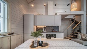 Una cocina moderna con una isla central, muebles blancos y una escalera que conduce a un nivel superior.