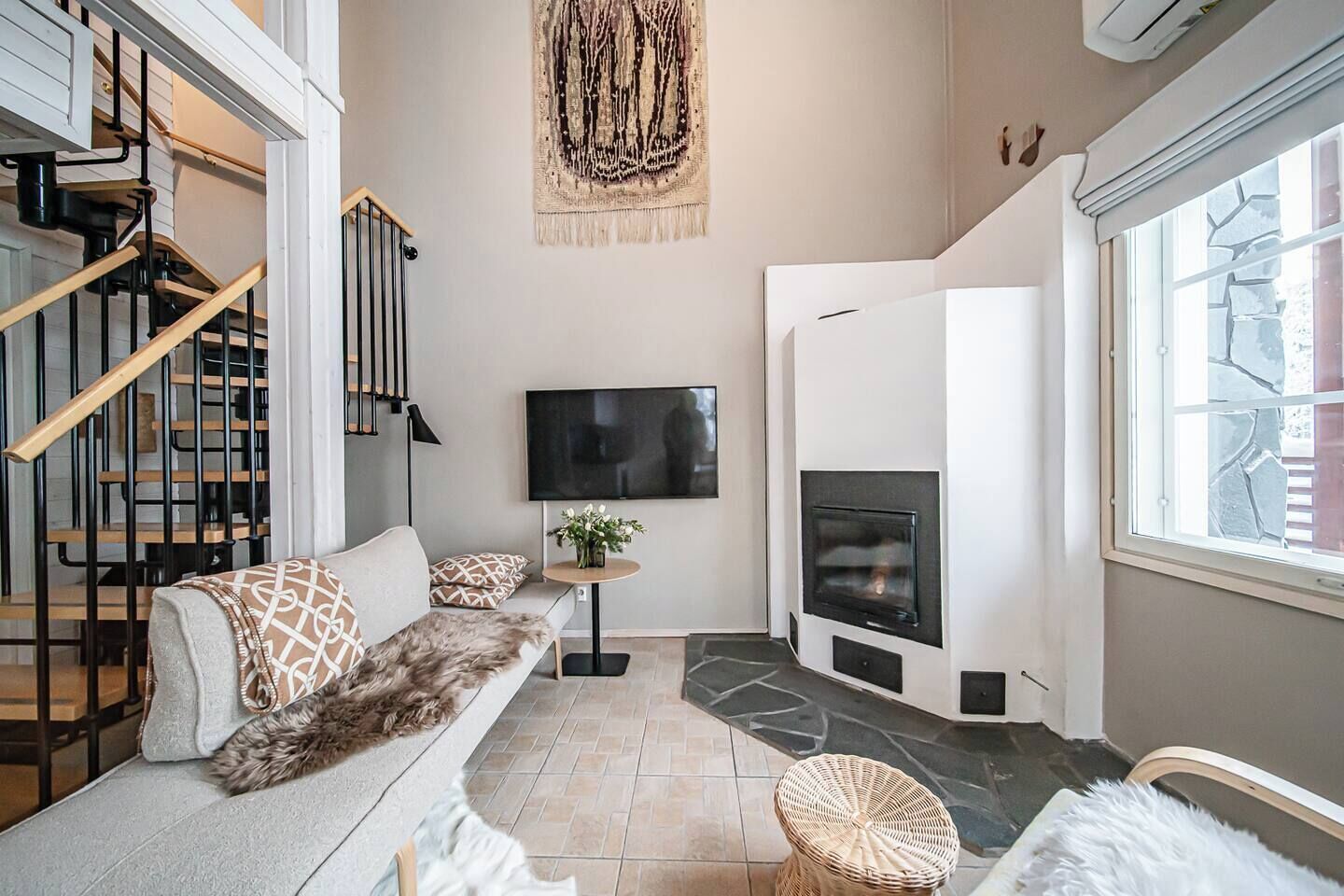Ein modernes Wohnzimmer mit Kamin, einer Couch mit gemusterten Kissen, einem Flachbildfernseher und einer Treppe mit Holzbeschlägen.