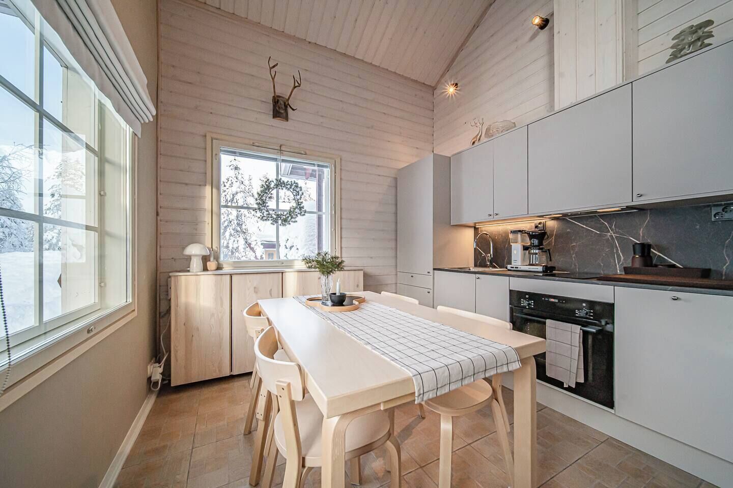 Una cucina moderna con mobili bianchi, un tavolo da pranzo in legno e una finestra decorata con un'asse di festoni.