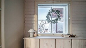 Una habitación con ventana, un banco de madera, una lámpara blanca y un adorno en el alféizar.