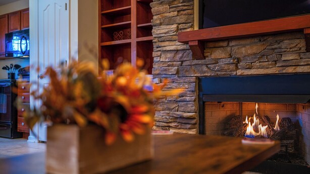 A cozy living room with a stone fireplace, a wooden coffee table, and a vase with autumn leaves.