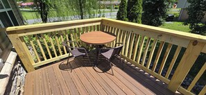 Eine Holzterrasse mit einem runden Tisch und zwei Stühlen, umgeben von einer Holzbrüstung.