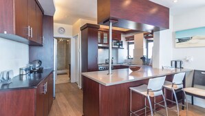 A modern kitchen with dark wood cabinets, stainless steel appliances, and a central island with bar stools. - Secure One Bed Uninterrupted Ocean Views (Cape Town)
