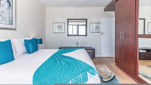 A bedroom with a bed, a wardrobe, a desk, and a window. - Secure One Bed Uninterrupted Ocean Views (Cape Town)