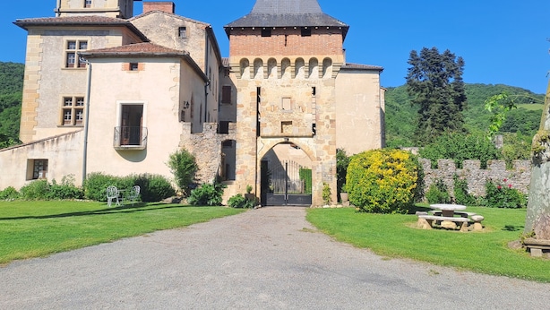 Eine historische Burg mit einem zentralen Turm, einem großen Bogenportal und einem umlaufenden Garten mit einem Picknicktisch.