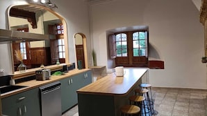 Eine Küche mit Holzarbeitsplatte, grünen Schränken, einer großen Kochinsel mit Barhocker und einem Fenster mit Blick auf Grünflächen.