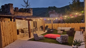 Eine Terrasse im Freien mit Steinmauern, Holzmöbeln und Lichterketten.