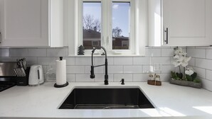 A modern kitchen with a white countertop, black faucet, and a window above the sink. - Modern Home Near Rosemont/allstate Arena O'hare 3 Bedroom Home (Des Plaines)