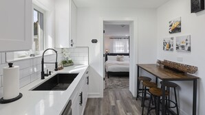 A compact kitchen with white cabinets, a black faucet, and a wooden dining table with bar stools. - Modern Home Near Rosemont/allstate Arena O'hare 3 Bedroom Home (Des Plaines)