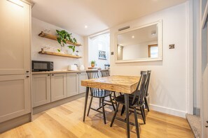 A modern kitchen with wooden cabinets, a dining table with chairs, and a microwave. - Lymington Sailor's Cottage/ hot tub /chef (Lymington)
