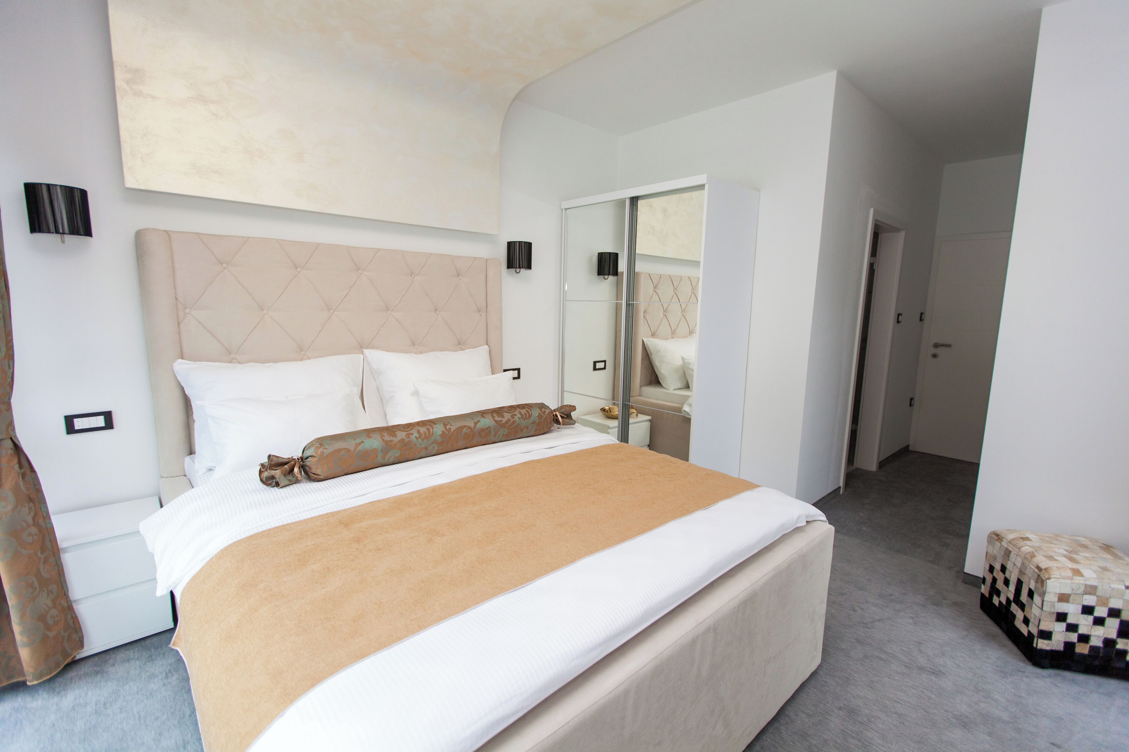 A modern hotel room with a large bed, a bedside table, a mirror, and a wardrobe.
